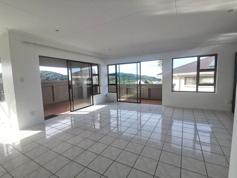 A bright, empty living area featuring white tiled floors, large sliding glass doors, and expansive windows that provide natural light and outdoor access.