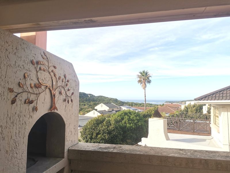 Covered balcony featuring a built-in braai and masonry balustrade, offering scenic views of the surrounding estate and distant coastline.