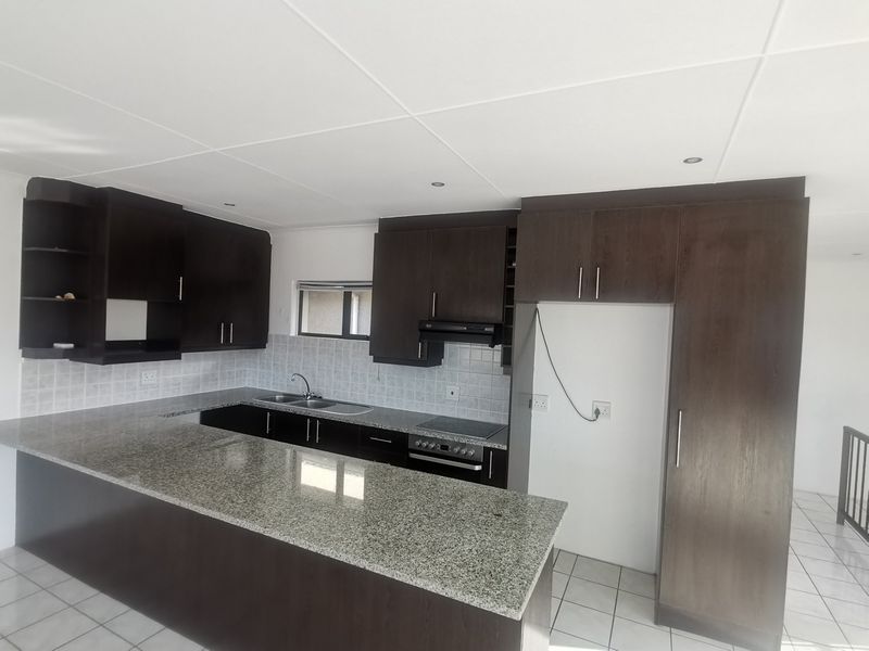 A clean, functional kitchen featuring dark wood cabinetry, granite countertops, a built-in hob with extractor, and tiled flooring throughout.