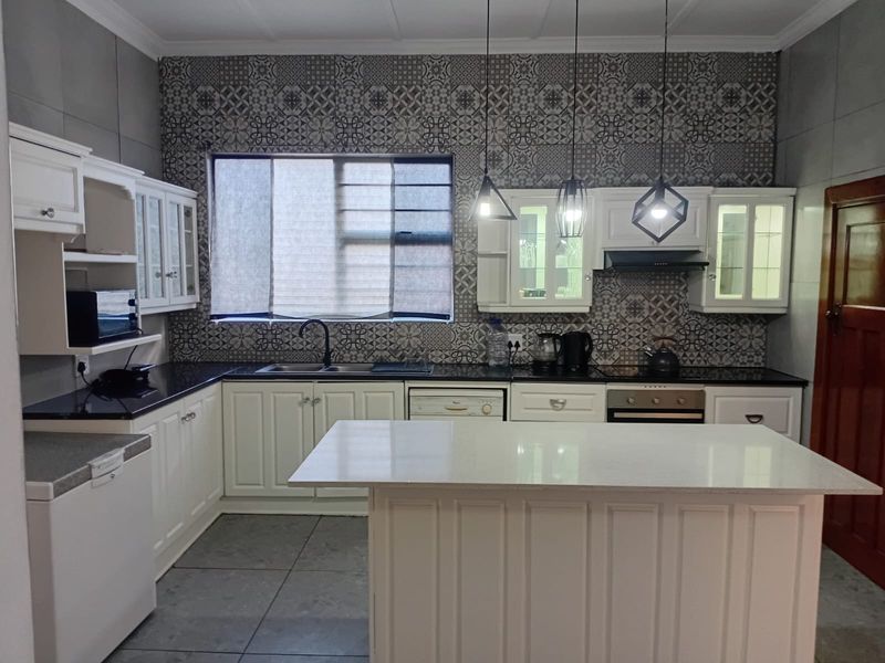 A well-appointed kitchen featuring white cabinetry, stone countertops, a central island, and a decorative tiled splashback with modern pendant lighting.