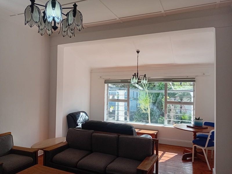 A bright living room featuring original hardwood flooring, large windows with natural light, and decorative ceiling details.