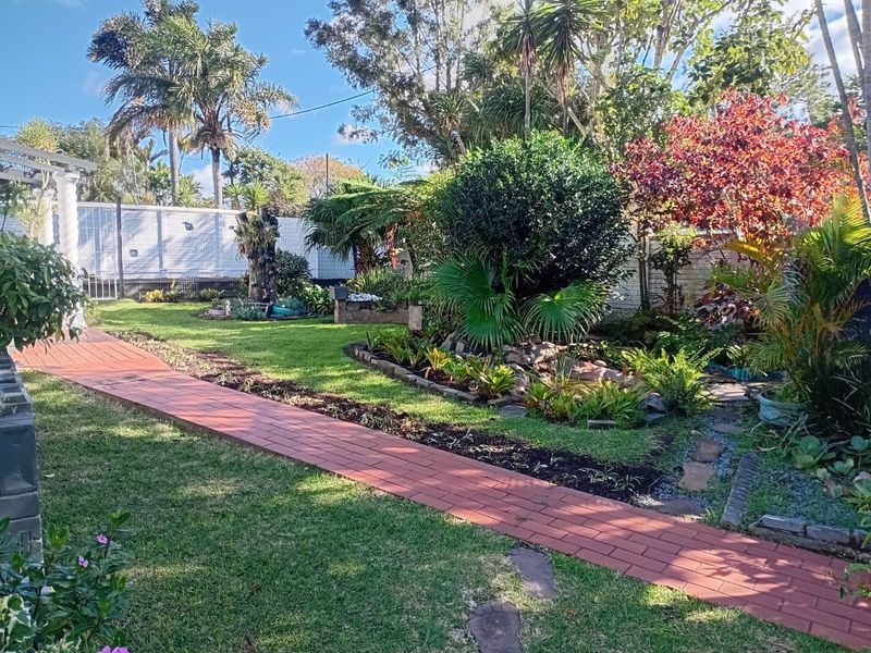 A well-maintained garden featuring a brick paved pathway, established landscaping, mature trees, and a stone-edged garden bed.