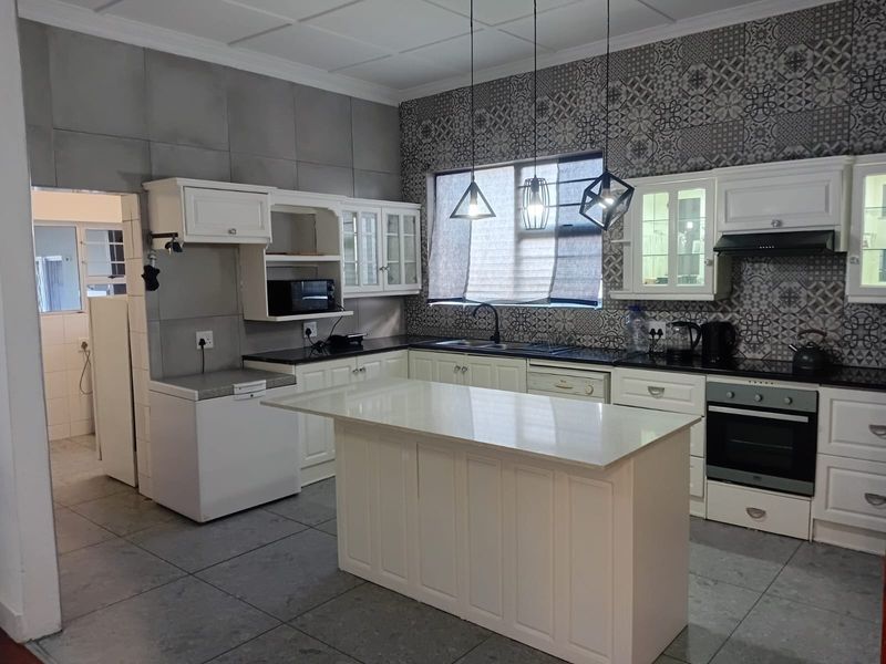 A well-appointed kitchen featuring a central island, built-in oven, extractor fan, and stylish patterned wall tiles with ample cabinetry for storage.
