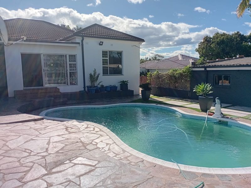 Rear exterior view featuring a swimming pool with a stone-paved patio area and access to the main dwelling.