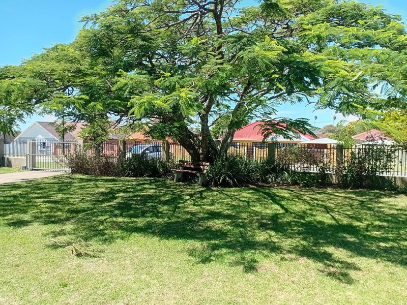 A well-maintained garden area featuring a large mature tree, manicured lawn, and secure metal perimeter fencing.