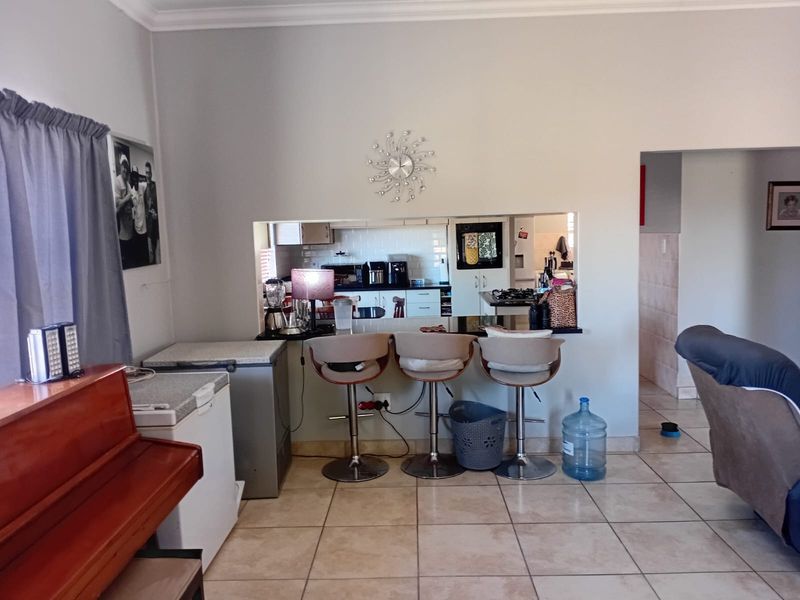 Open plan living area featuring a breakfast bar pass-through window connecting to a functional kitchen with built-in cabinetry and tiled flooring.