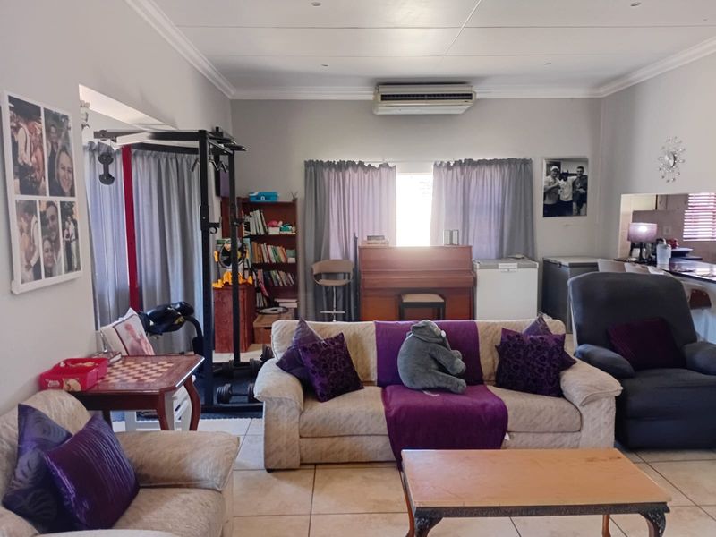 Open-plan living area featuring tiled flooring, ceiling coving, and a wall-mounted air conditioning unit, providing a versatile space for relaxation and daily activities.