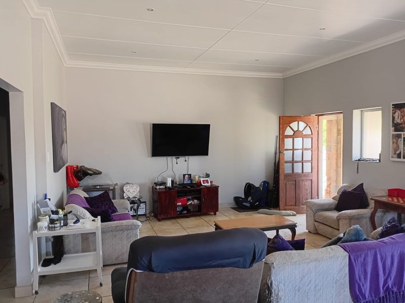 A spacious living room featuring tiled flooring, recessed ceiling lights, and a timber panelled door leading to the exterior.