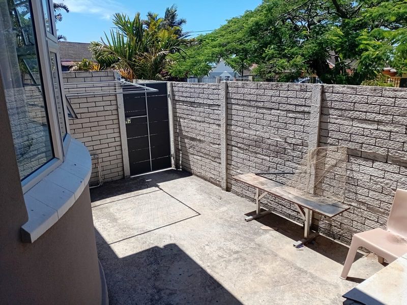 A private rear courtyard area featuring a concrete patio, secure boundary walling, and a metal pedestrian gate.