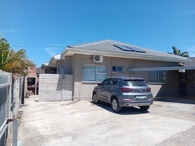 Front exterior view of the house featuring a concrete driveway, carport, built-in braai area, and solar water heating panels on the roof.