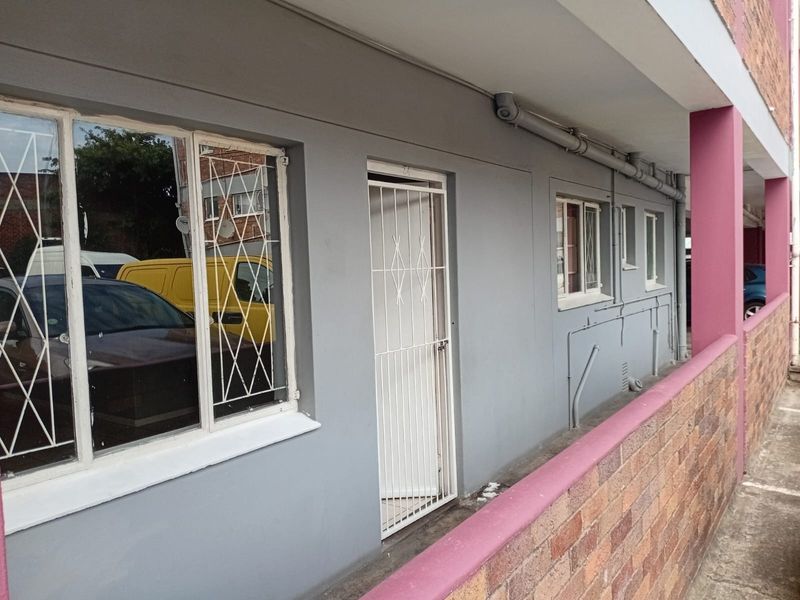 Exterior view of an apartment entrance featuring a security gate, metal-framed windows, and a brick parapet wall along the walkway.