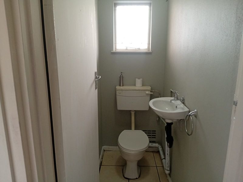 A compact guest bathroom featuring a standard toilet and wall-mounted basin with tiled flooring and a small window for natural light.