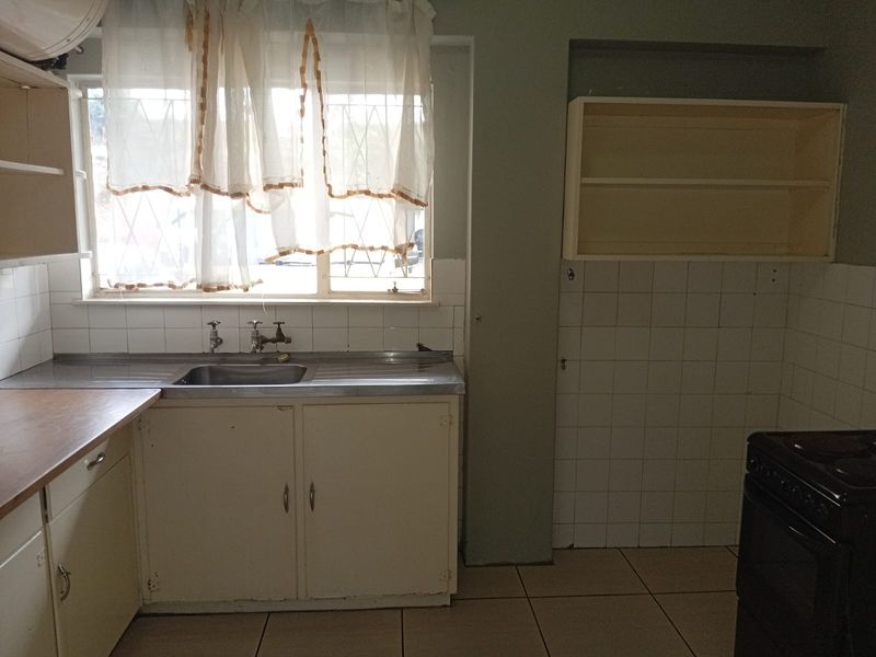 A functional kitchen space featuring a stainless steel sink, tiled splashback, and built-in cabinetry, offering a blank canvas for renovation and modernization.