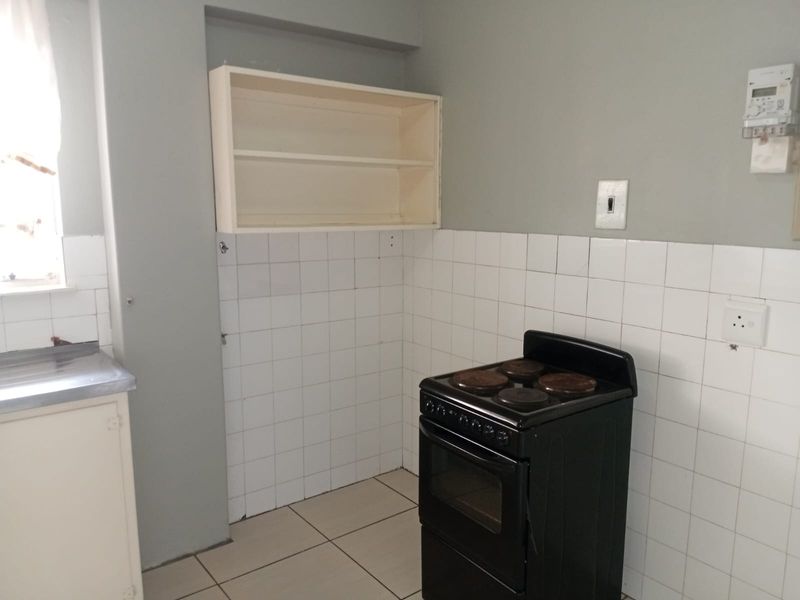 A functional kitchen area featuring a tiled splashback, built-in shelving, and an electric stove, offering a blank canvas for potential renovation and modernization.
