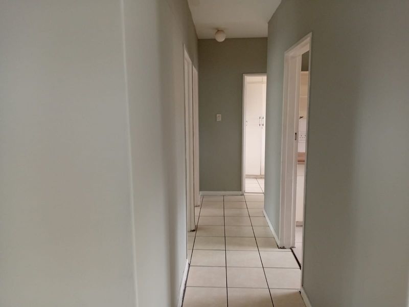 A clean, neutral-toned hallway featuring tiled flooring and access to multiple rooms, providing a functional transition space within the apartment.