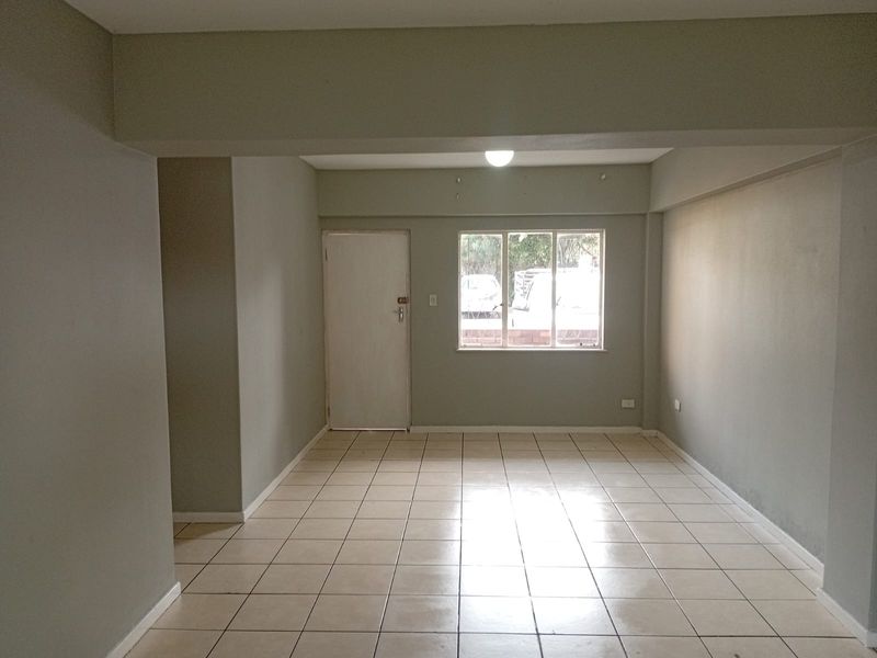 An empty, open-plan living area featuring neutral wall paint, ceramic floor tiles, and a window with security bars.