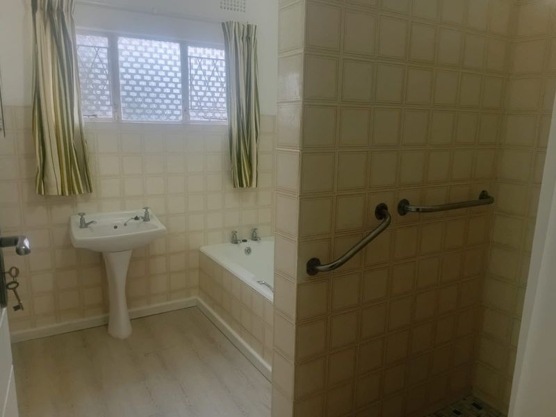 A dated bathroom featuring a pedestal basin, built-in bathtub, and tiled walls with installed grab rails.
