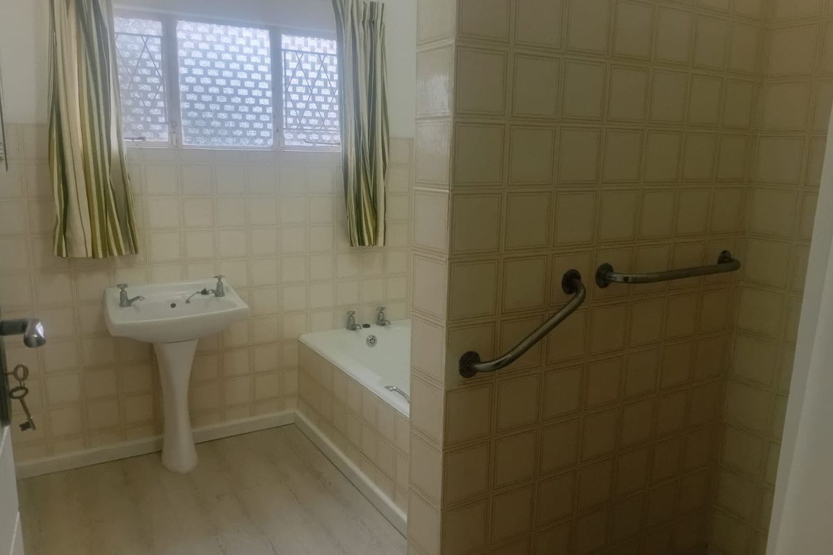 A dated bathroom featuring a pedestal basin, built-in bathtub, and tiled walls with installed grab rails.