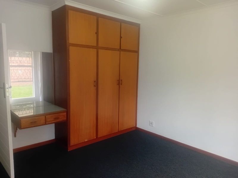 A bedroom featuring built-in wooden cupboards with an integrated vanity unit, carpeted flooring, and neutral wall finishes.