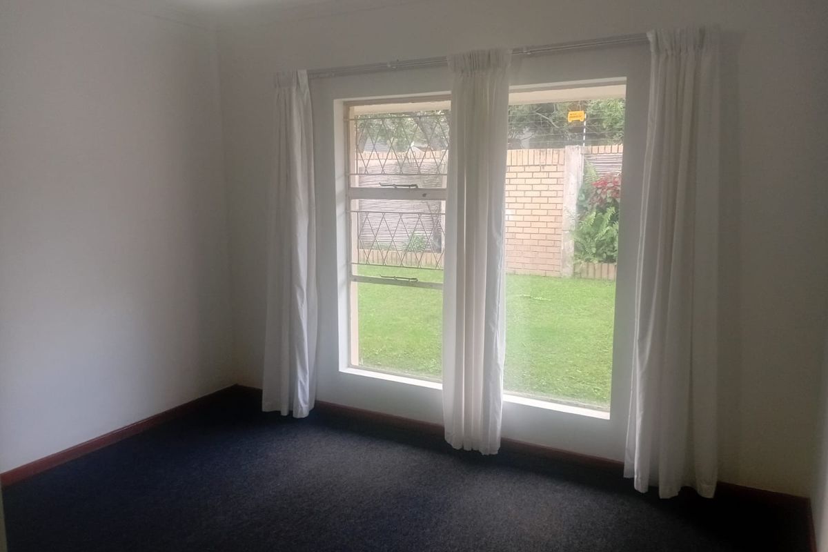 A vacant bedroom featuring carpeted flooring, large windows with security bars, and neutral white walls, offering a blank canvas for personalization.