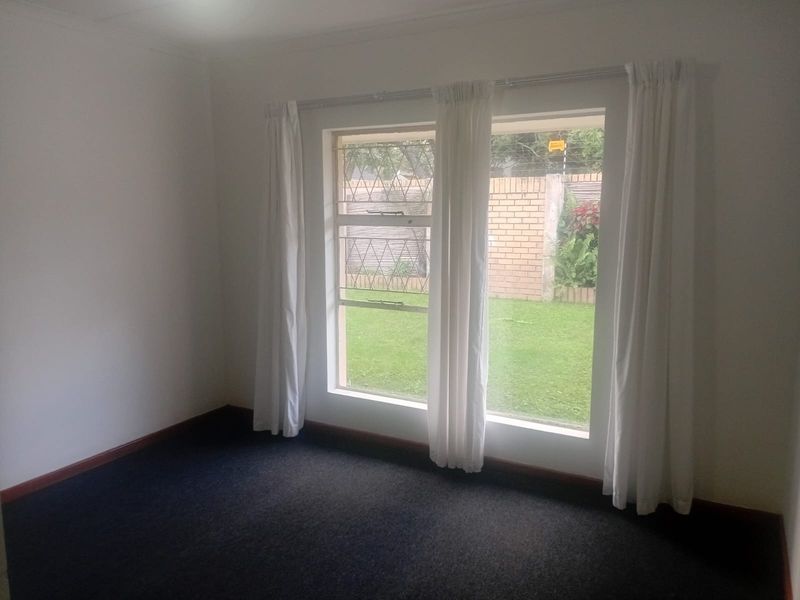 A vacant bedroom featuring carpeted flooring, large windows with security bars, and neutral white walls, offering a blank canvas for personalization.