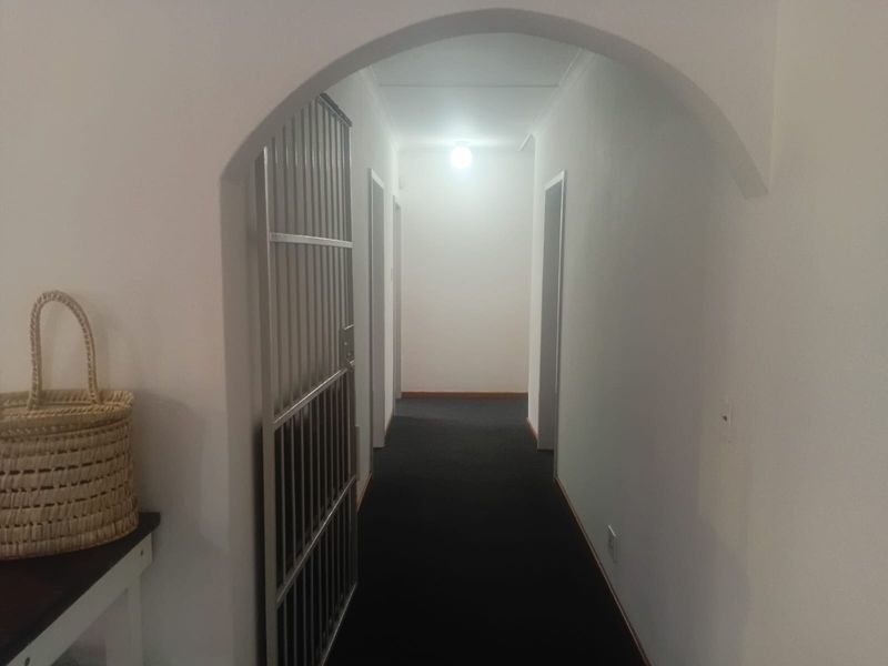 A functional hallway featuring an arched entrance, dark carpeting, and a fitted security gate providing access to the interior living spaces.