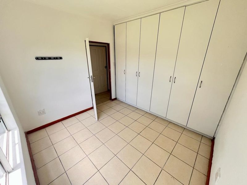 A vacant bedroom featuring neutral tiled flooring and extensive built-in cupboard storage, offering a clean and functional space ready for personalization.