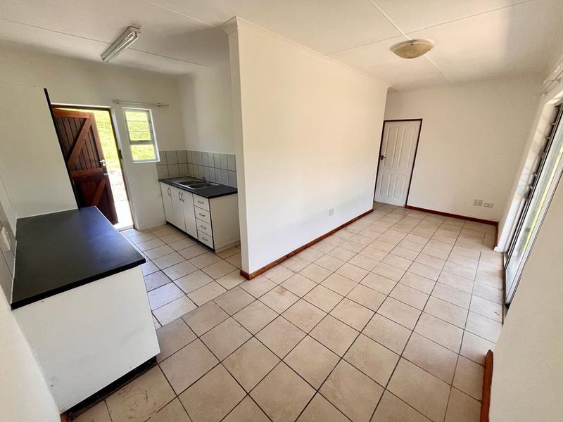 An open-plan living and kitchen area featuring tiled flooring, built-in cabinetry with laminate countertops, and access to the exterior via a sliding glass door.