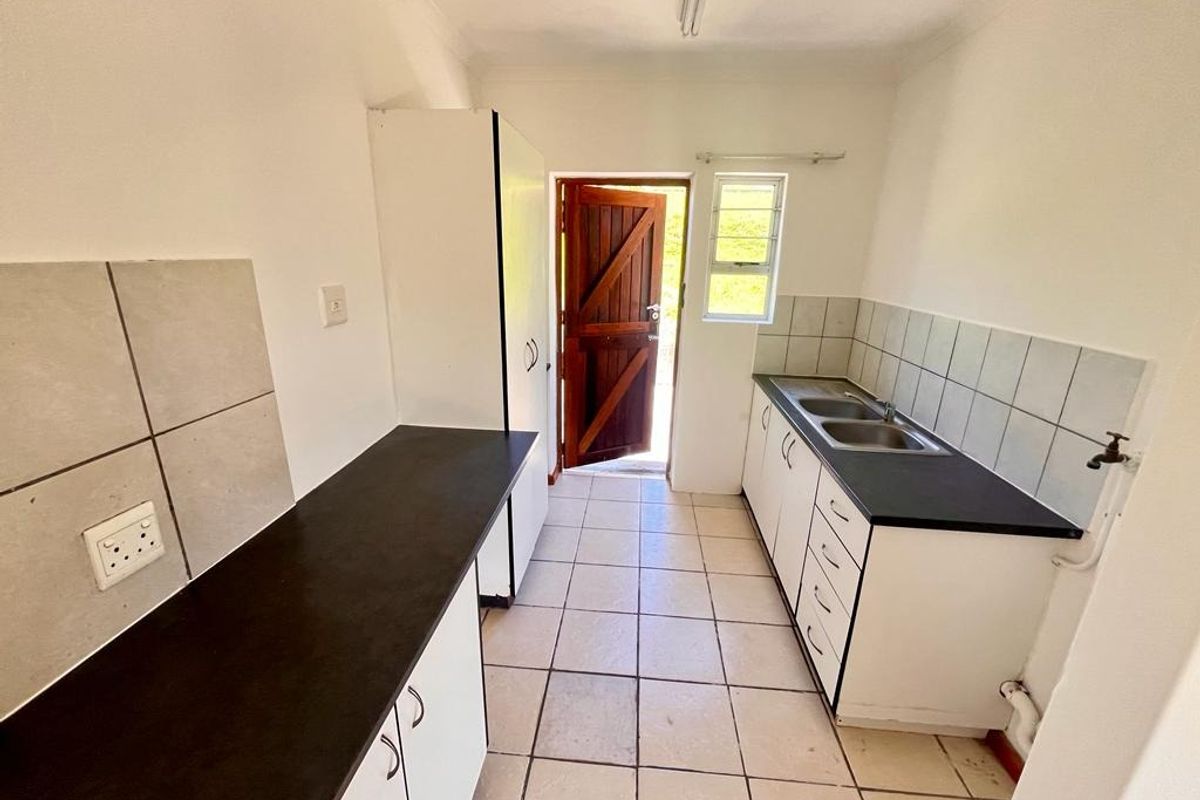 A functional scullery area featuring built-in cabinetry, double sink, tiled splashbacks, and direct access to the exterior.