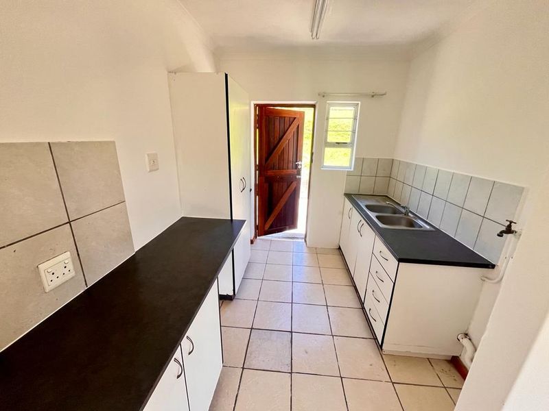 A functional scullery area featuring built-in cabinetry, double sink, tiled splashbacks, and direct access to the exterior.