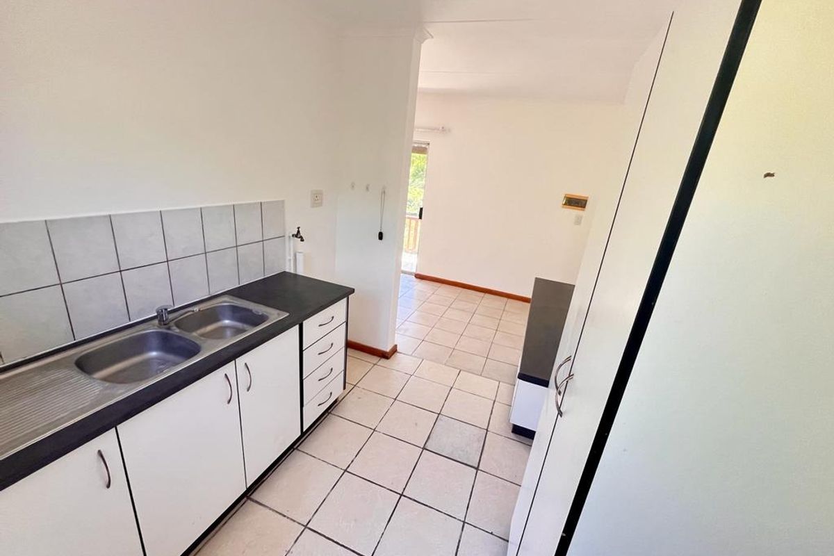 A functional kitchen area featuring built-in cabinetry, a double basin sink, and tiled flooring, leading into an adjacent living space.