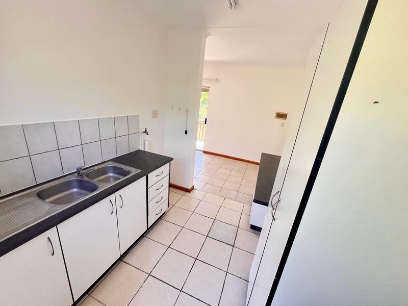 A functional kitchen area featuring built-in cabinetry, a double basin sink, and tiled flooring, leading into an adjacent living space.