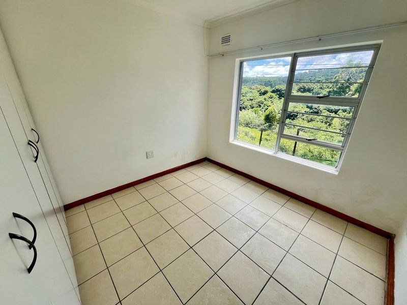A vacant bedroom featuring tiled flooring, built-in cupboards, and a large window with scenic views.