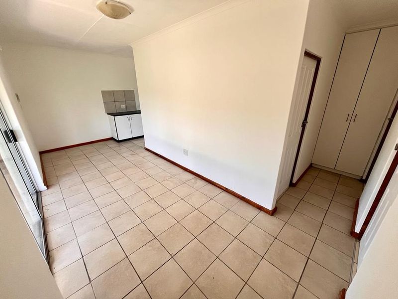 An open-plan living area featuring tiled flooring, a compact kitchenette with built-in cabinetry, and access to a sliding glass door.