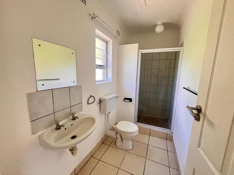 A functional bathroom featuring a pedestal basin, toilet, and a separate shower enclosure with tiled flooring.