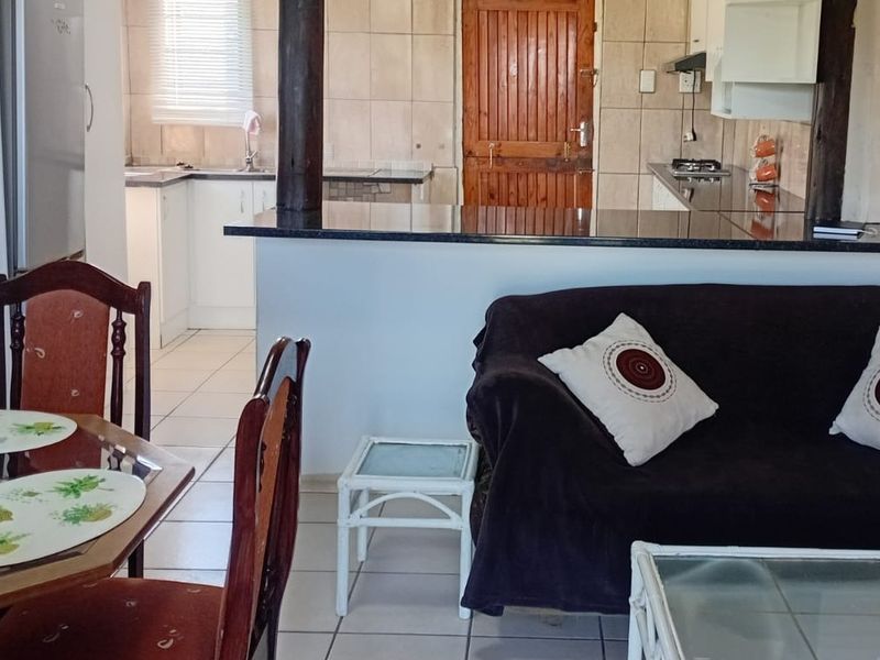 Open-plan living and kitchen area featuring a granite breakfast bar, tiled flooring, and functional kitchen cabinetry with a gas hob and extractor fan.