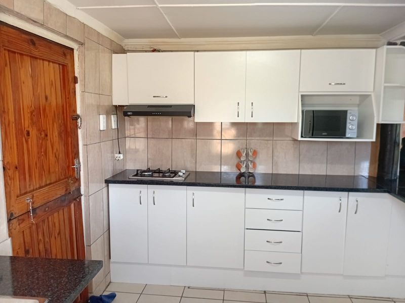 A functional kitchen featuring white cabinetry, dark granite countertops, a gas hob, extractor fan, and built-in microwave with tiled splashbacks.