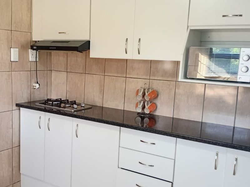 A functional kitchen featuring white cabinetry, dark granite countertops, a gas hob with extractor fan, and neutral tiled backsplash.