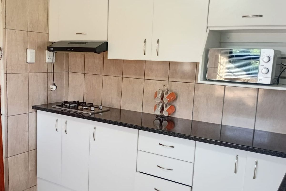 A functional kitchen featuring white cabinetry, dark granite countertops, a gas hob with extractor fan, and neutral tiled backsplash.