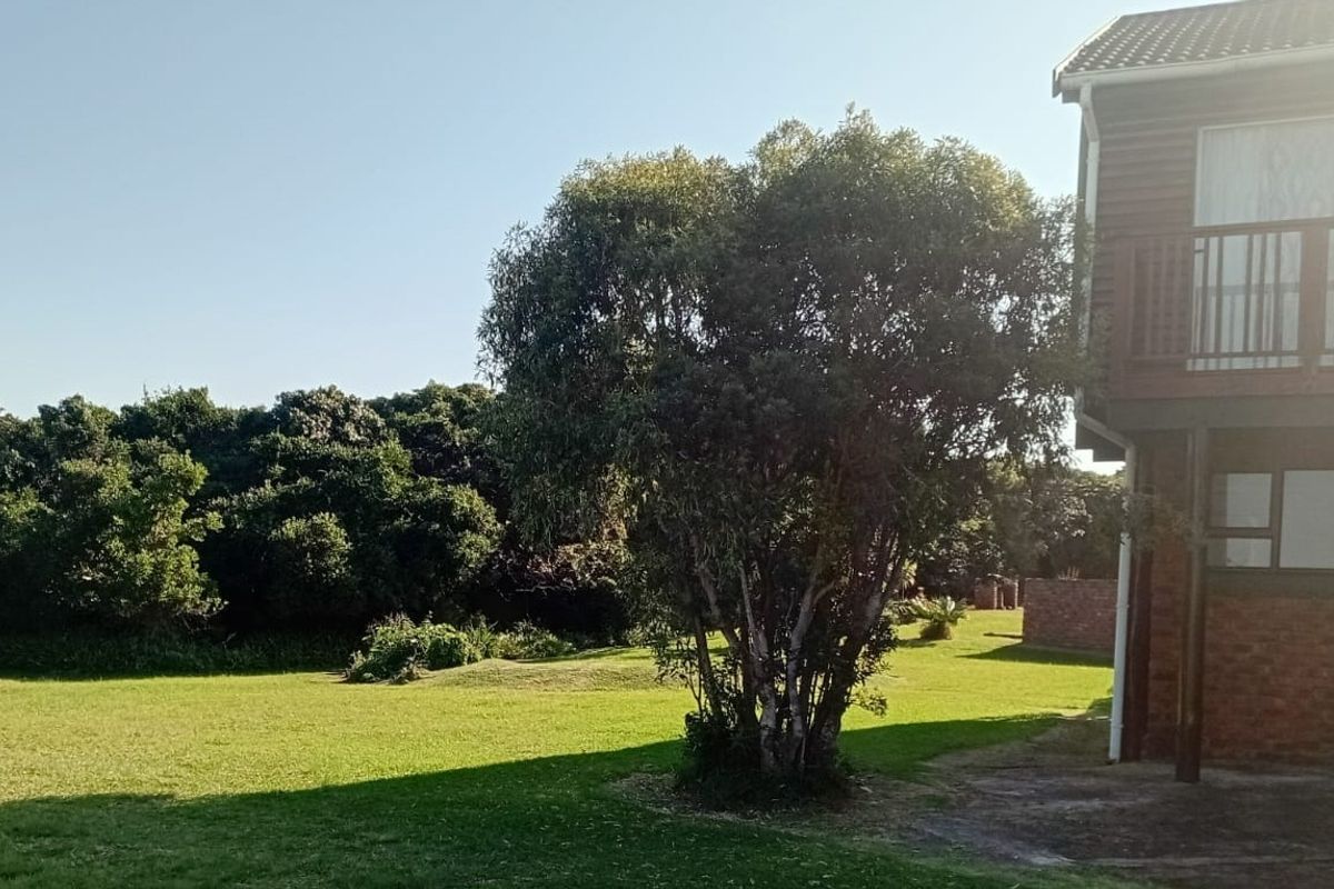 Rear view of the property featuring a brick facade, a timber balcony with railing, and a spacious garden area with established trees.