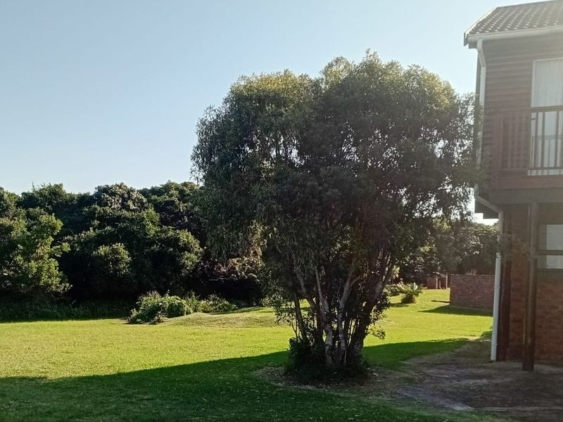 Rear view of the property featuring a brick facade, a timber balcony with railing, and a spacious garden area with established trees.