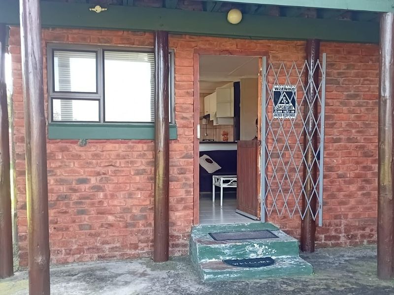 Exterior view of a brick-faced flat entrance featuring timber support posts, a security gate, and a concrete step leading into the living area.