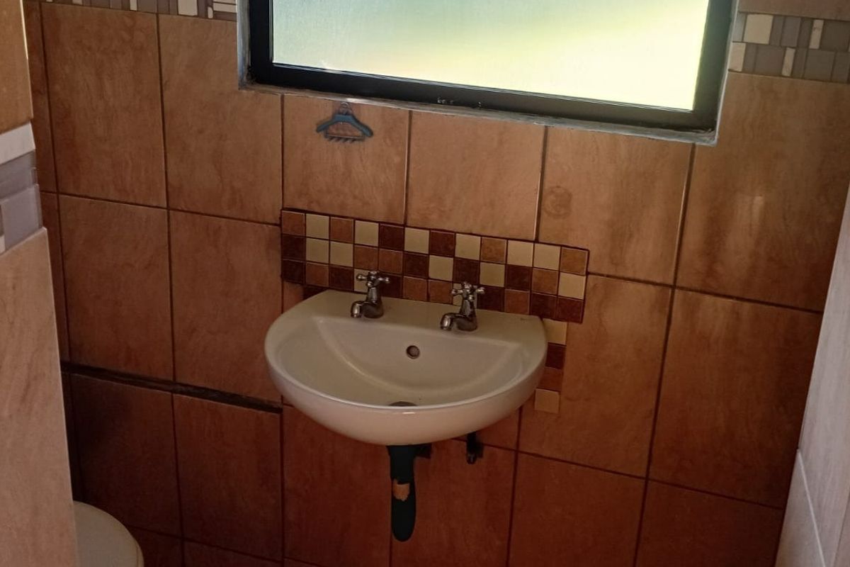 A compact bathroom featuring a wall-mounted basin with dual-handle taps and decorative tiled splashback, set against full-height ceramic wall tiling.