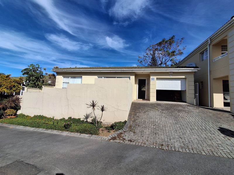 Front elevation of a townhouse featuring a paved driveway, single garage, and a boundary wall with visible plaster cracking.