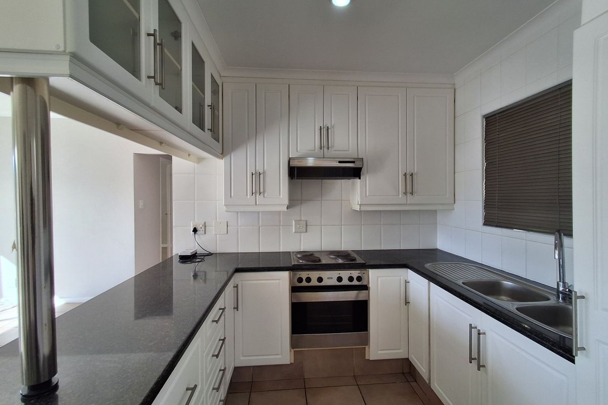 A clean, well-maintained kitchen featuring white cabinetry, dark granite countertops, integrated stainless steel appliances, and a tiled backsplash.