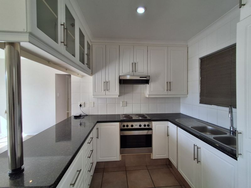 A clean, well-maintained kitchen featuring white cabinetry, dark granite countertops, integrated stainless steel appliances, and a tiled backsplash.