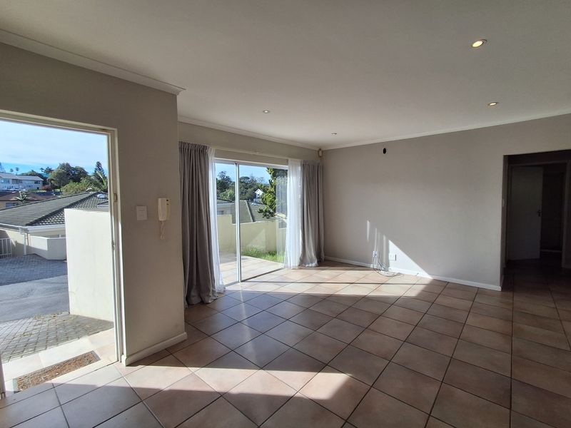 Spacious, light-filled living area featuring neutral tiled flooring, recessed downlights, and direct access to an outdoor patio through sliding glass doors.