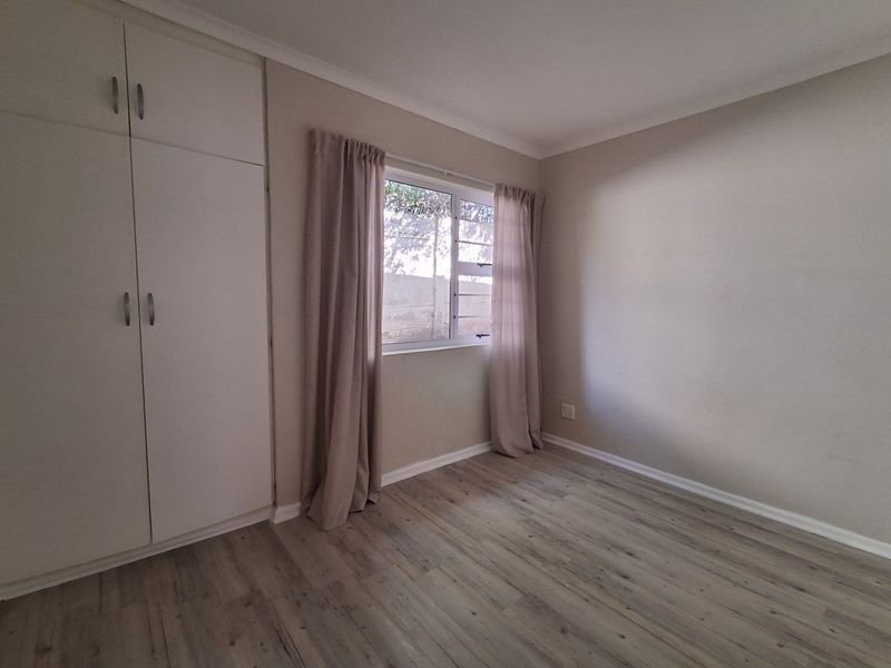 A clean, empty bedroom featuring light-toned laminate flooring, neutral walls, and built-in storage cupboards.