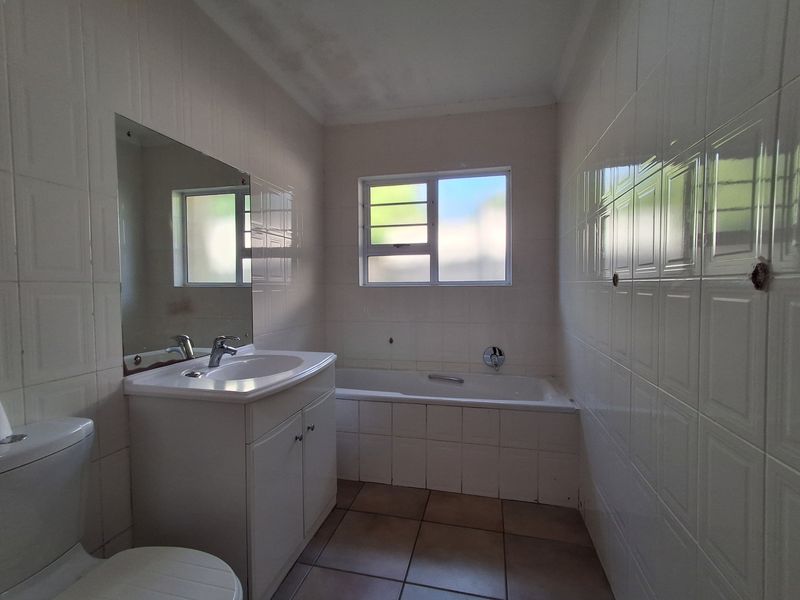 A functional bathroom featuring a built-in vanity, bathtub, and full-height wall tiling, offering a clean canvas for potential cosmetic updates.