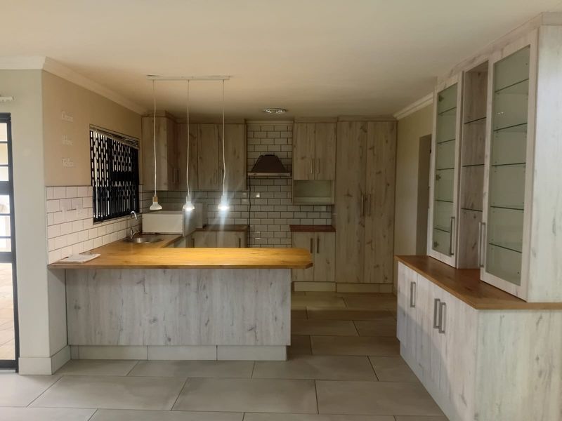 Modern kitchen featuring light wood-grain cabinetry, wooden countertops, subway tile backsplash, and a functional breakfast bar layout with integrated lighting.